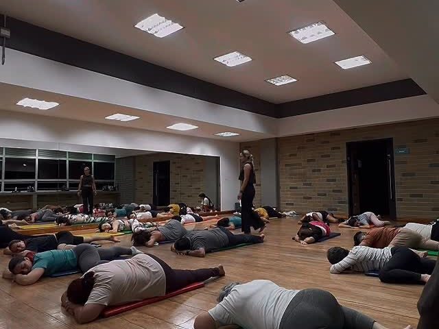 Práctica de relajación profunda: personas descansando sobre sus tapetes en un salón de piso de madera con luz suave.
